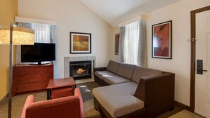A modern hotel room with a sofa, a TV, a fireplace, and artwork on the walls. - SenS Suites Livermore, SureStay Collection by Best Western (Livermore)