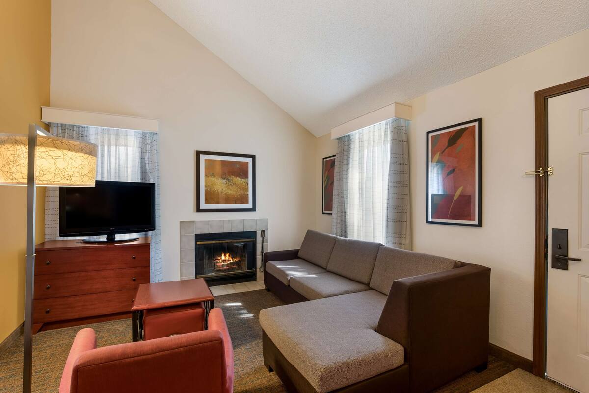 A modern hotel room with a sofa, a TV, a fireplace, and artwork on the walls.