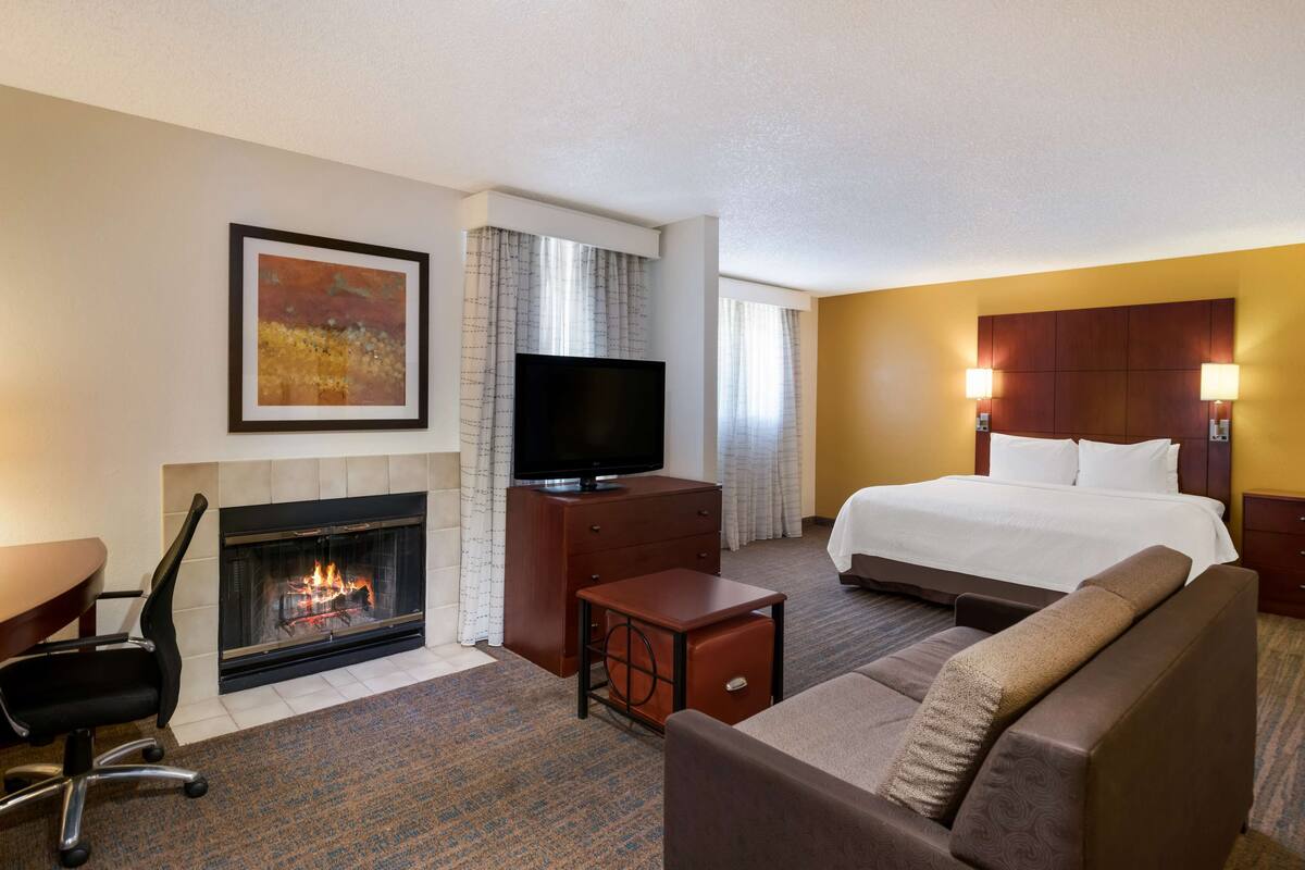 A hotel room with a fireplace, a bed, a sofa, a desk, and a television.