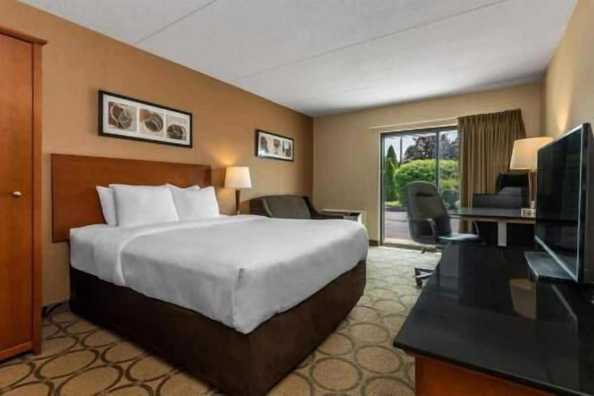 A hotel room with a bed, a desk with a TV, a chair, and a door.
