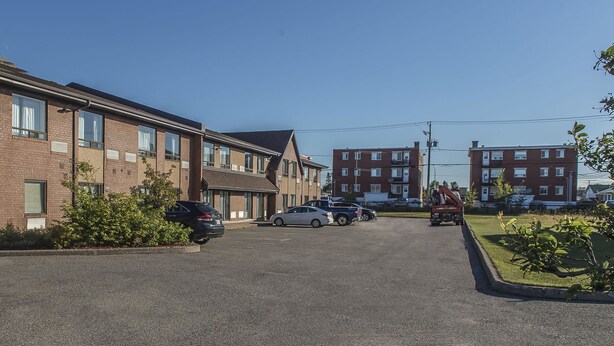 A parking lot with cars and a fire truck, surrounded by multi-story brick buildings with windows and a clear sky.