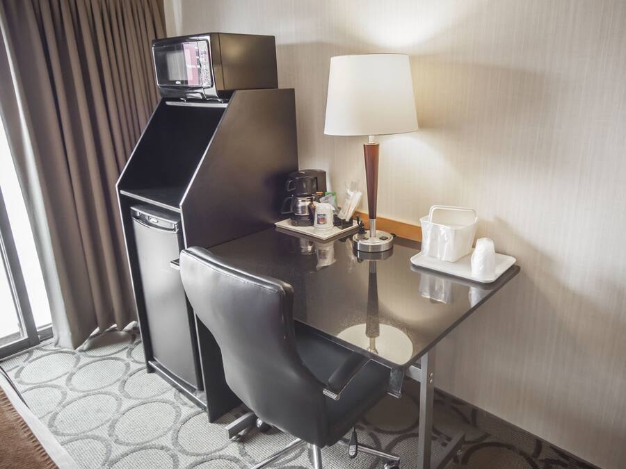 Habitación de hotel con un escritorio pequeño, cafetera, lámpara y una mesita con tazas y una botella.