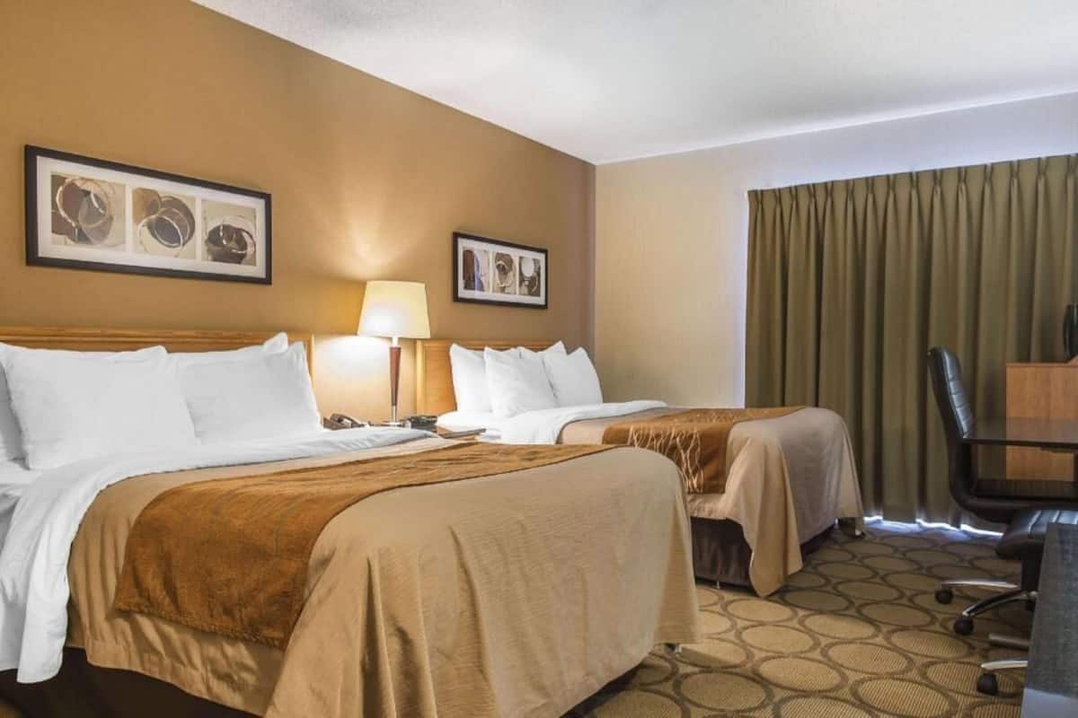 A hotel room with two beds, a desk, a chair, and two framed pictures on the wall.