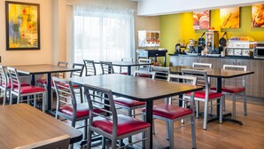 A modern dining area with multiple tables and chairs, a kitchen counter with appliances, and a large window with sheer curtains.