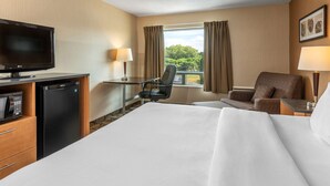 A hotel room with a bed, a desk, a chair, a television, and a refrigerator.