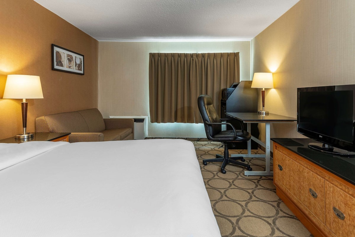 A hotel room with a large bed, a desk with a chair, a television, and two lamps.