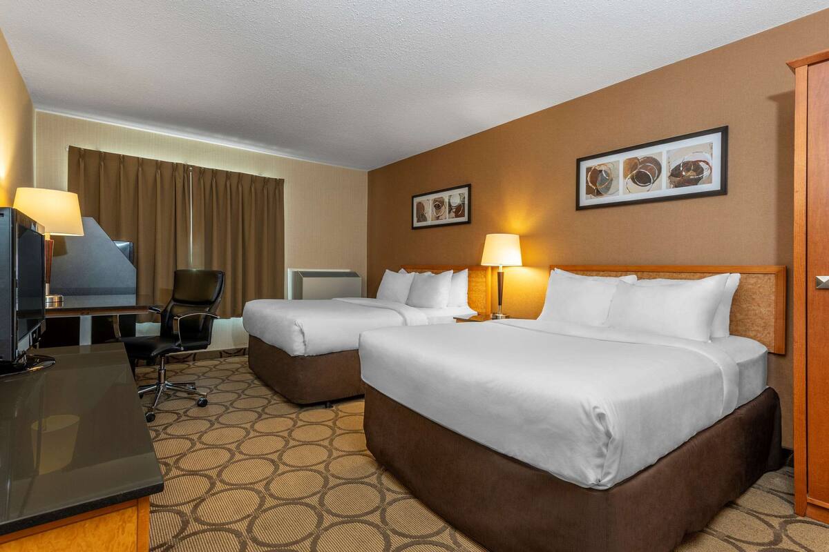 A hotel room with two beds, a desk, a TV, and a chair.