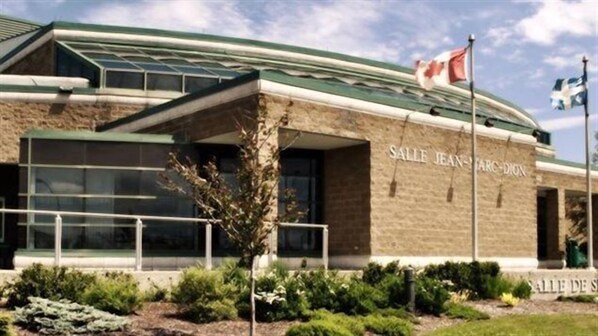 A building with a sign reading "SALLE JEAN-ARC-DION" and a Canadian flag.