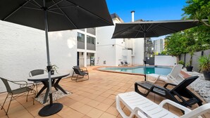Un espace aménagé au bord de la piscine, avec une table et des chaises, deux parasols et des chaises longues.