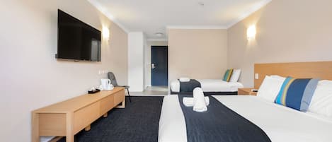 A hotel room with a large bed, a smaller bed, a desk with a chair, a flat-screen TV mounted on the wall, and a door leading to another room.