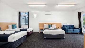 A hotel room with two single beds, a sofa, a desk, and a window.