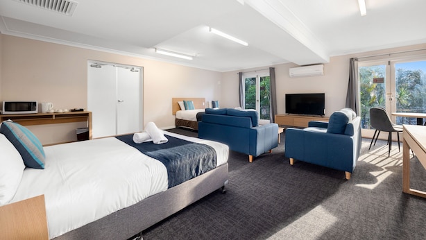 Une chambre d’hôtel moderne dotée d’un grand lit, de deux canapés, d’un bureau, d’une télévision et offrant une vue sur l’extérieur.