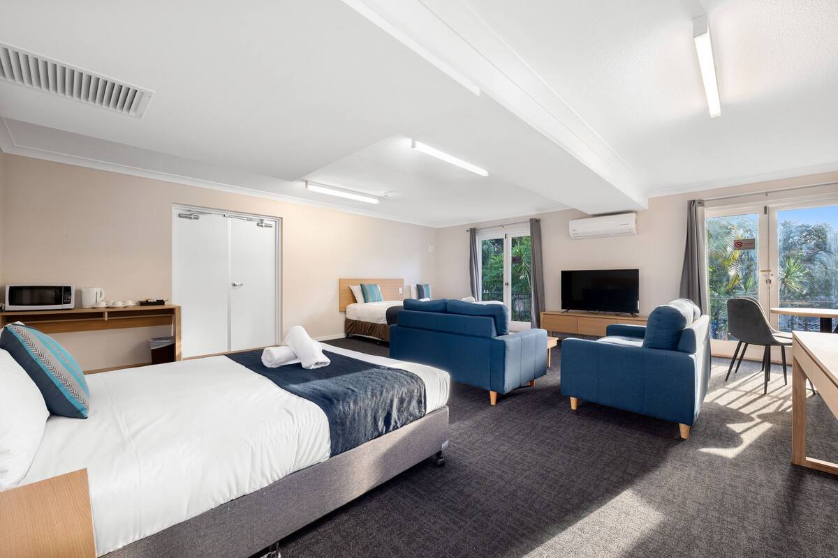 Une chambre d’hôtel moderne dotée d’un grand lit, de deux canapés, d’un bureau, d’une télévision et offrant une vue sur l’extérieur.