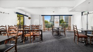 Une salle de conférence avec des chaises et des tables en bois, de grandes fenêtres avec des rideaux et une vue sur les bâtiments environnants.