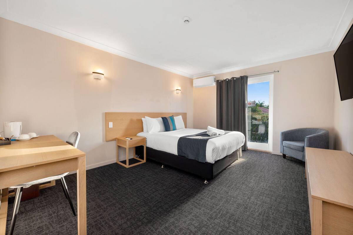 Une chambre d’hôtel avec un lit, un bureau, une chaise, une petite table et une fenêtre avec des rideaux.