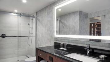 Un baño moderno con ducha de vidrio, un espejo grande y un mostrador negro con lavamanos.