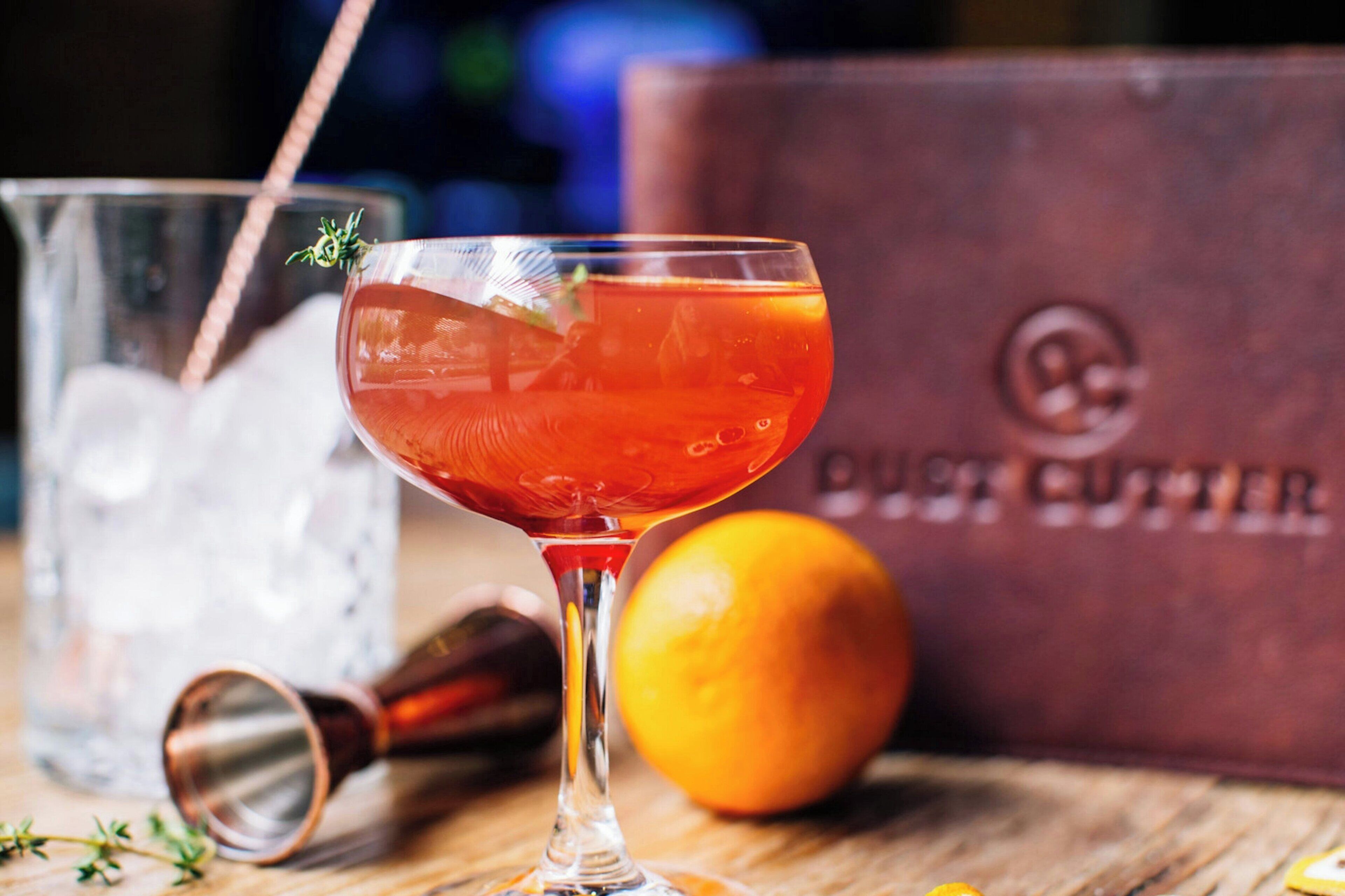 Um copo de cocktail com canudo, um coqueteleira de cobre e um limão sobre uma superfície de madeira.