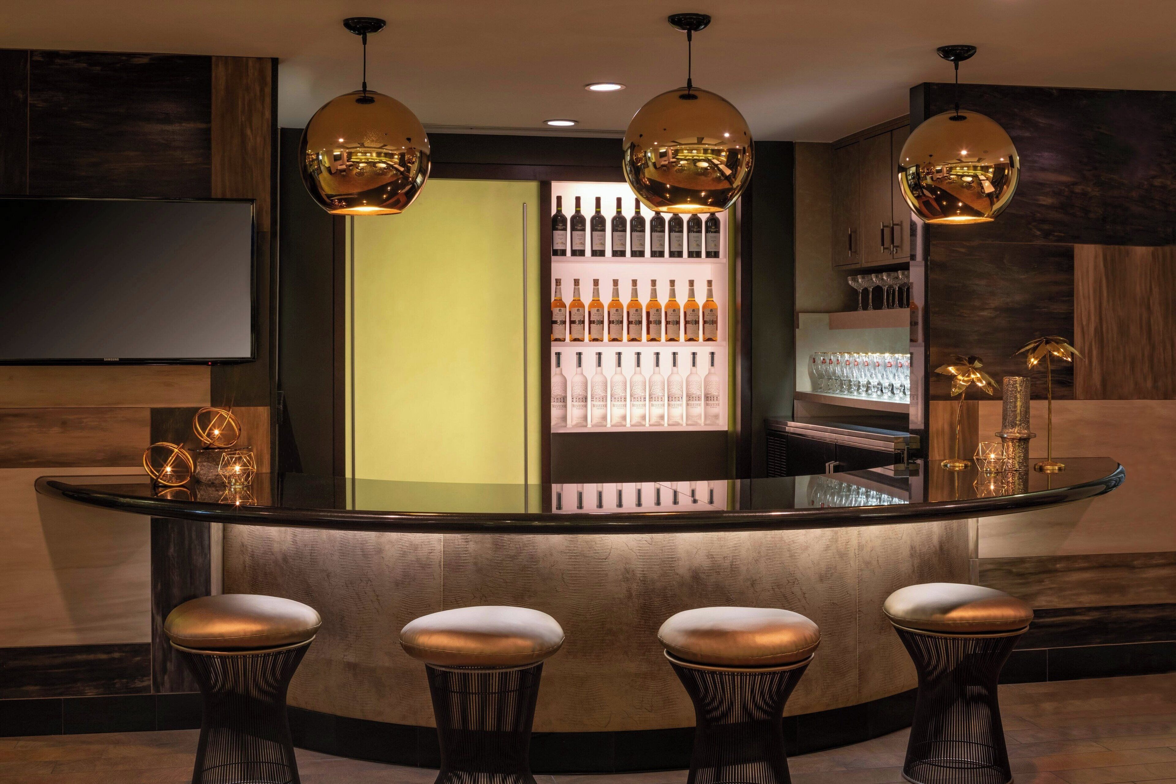 A bar area with a curved counter, three stools, and a shelf of bottles.