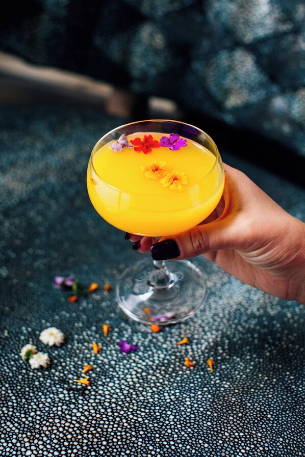 Eine Hand hält ein Cocktailglas mit einem gelben Getränk und einer Blütenverzierung.