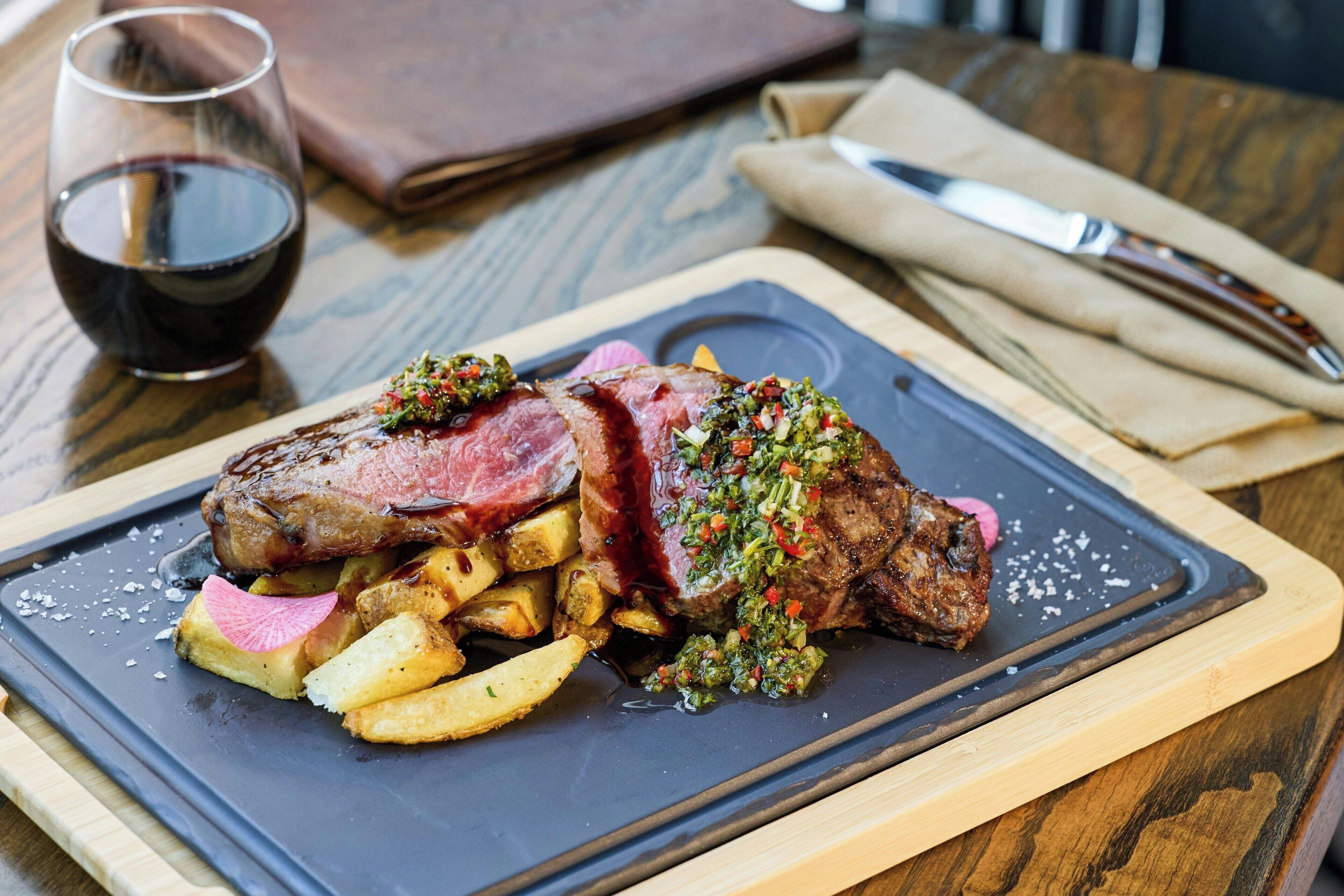 Un plato de carne con papas fritas y una copa de vino tinto sobre una mesa de madera.