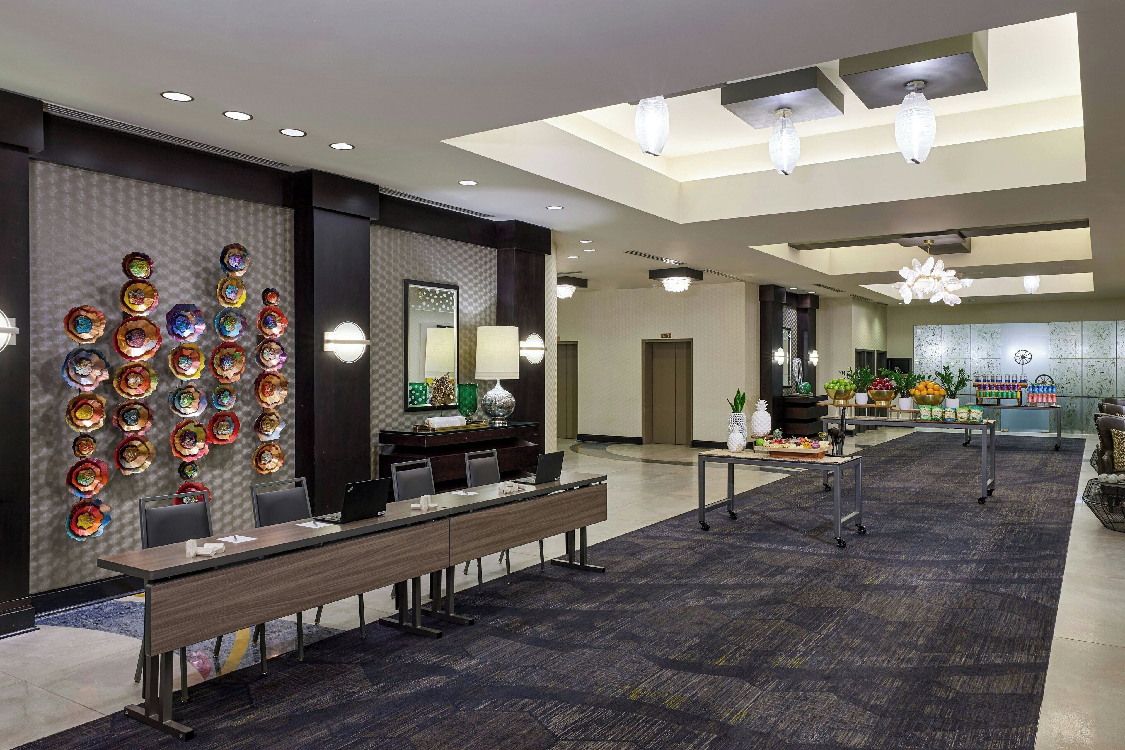 Un lobby moderno de hotel con una larga recepción, una pared de platos decorativos de colores y una exhibición de frutas.