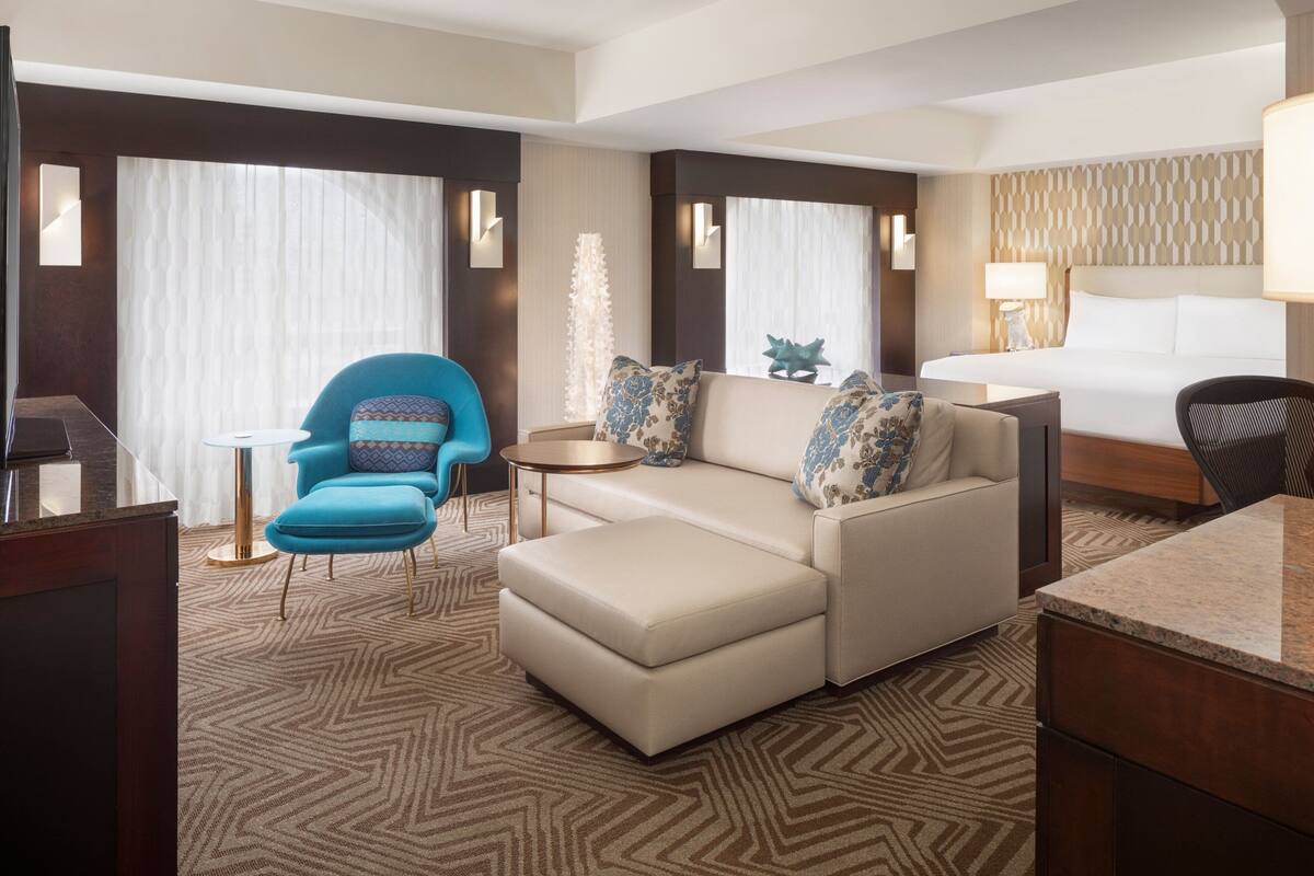 Une chambre d’hôtel avec un grand lit, un canapé, un fauteuil, une petite table et un bureau.