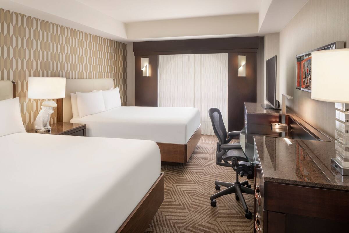 Une chambre d’hôtel avec deux lits, un bureau, une chaise et un téléviseur.
