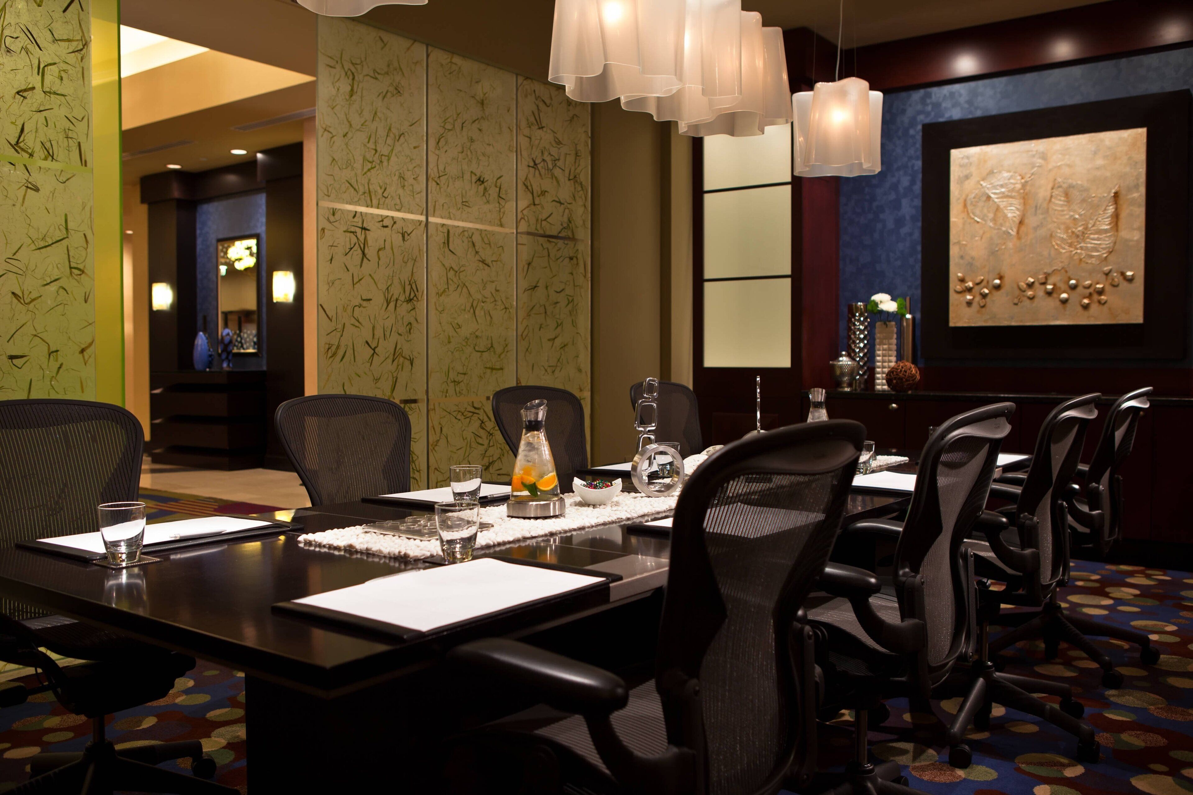 A conference room with a long table, multiple chairs, and a decorative wall piece.