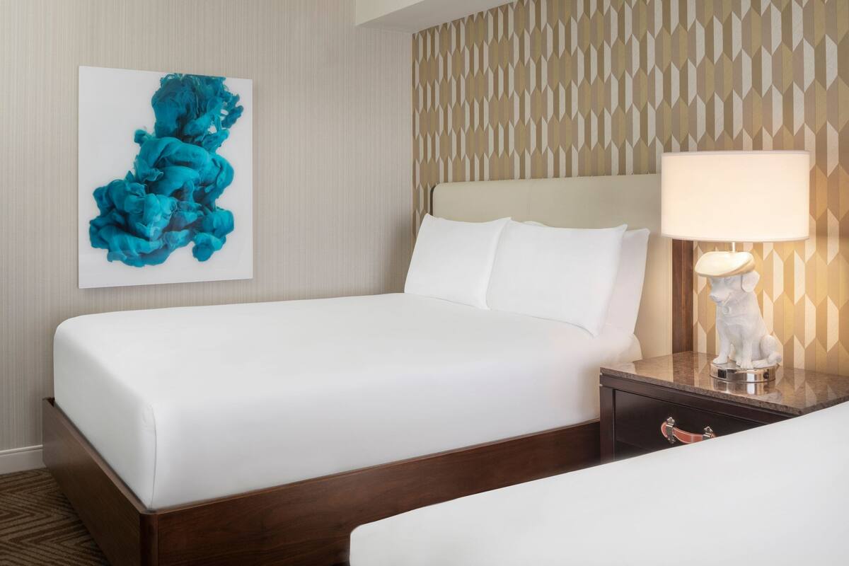 Une chambre d’hôtel avec un lit, une table de chevet avec une lampe et une œuvre d’art murale.