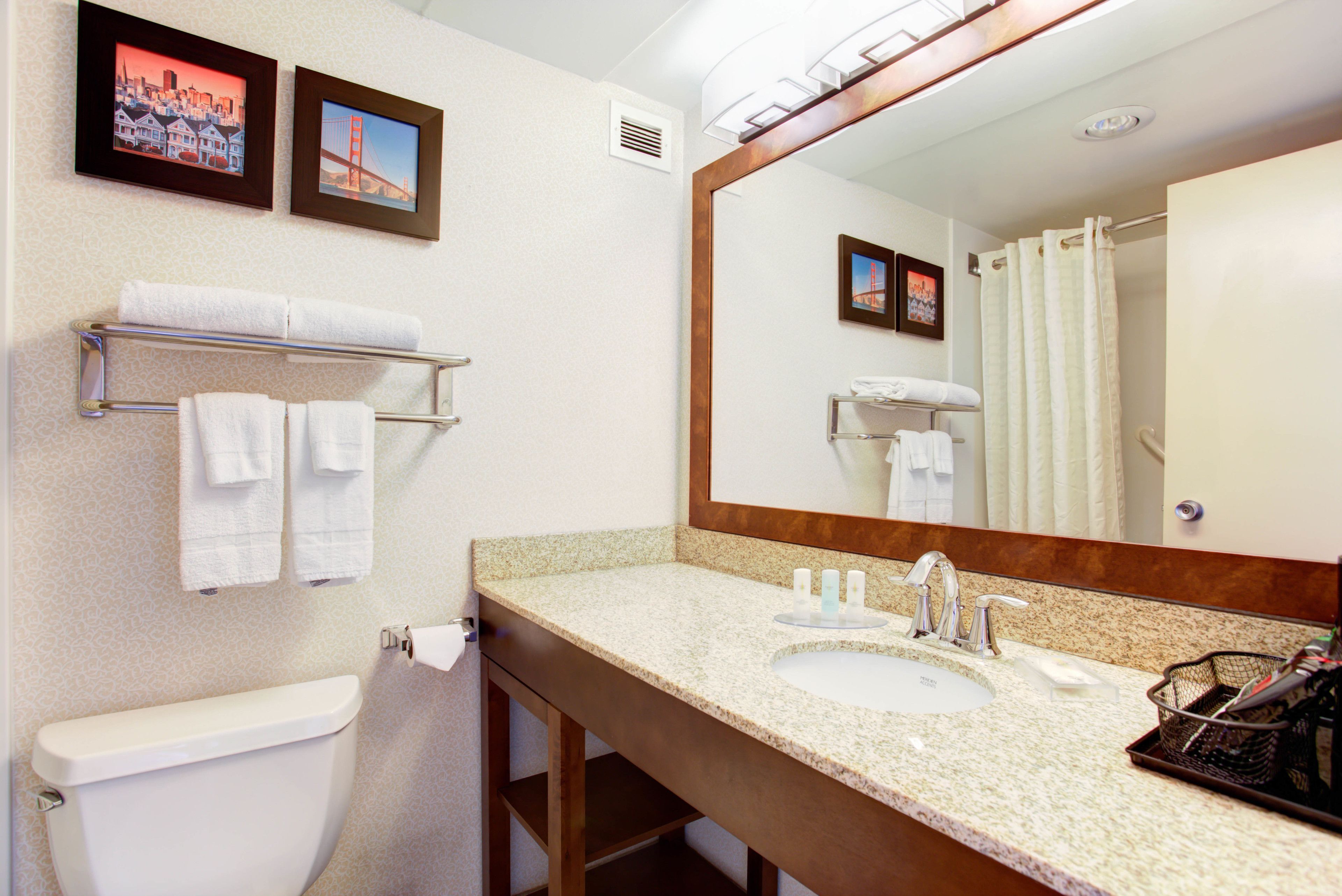 A bathroom with a toilet, sink, and mirror. There are towels on a rack and a shower curtain.