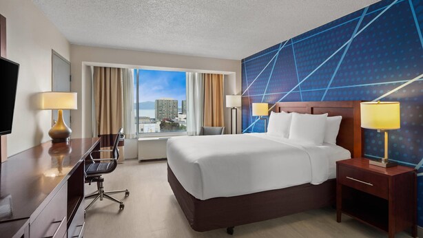 A hotel room with a large bed, a desk with a chair, a TV, and a view of the city. - Comfort Inn by the Bay (San Francisco)