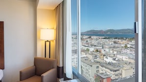 A hotel room with a large window offering a cityscape view, a lamp, and a chair. - Comfort Inn by the Bay (San Francisco)