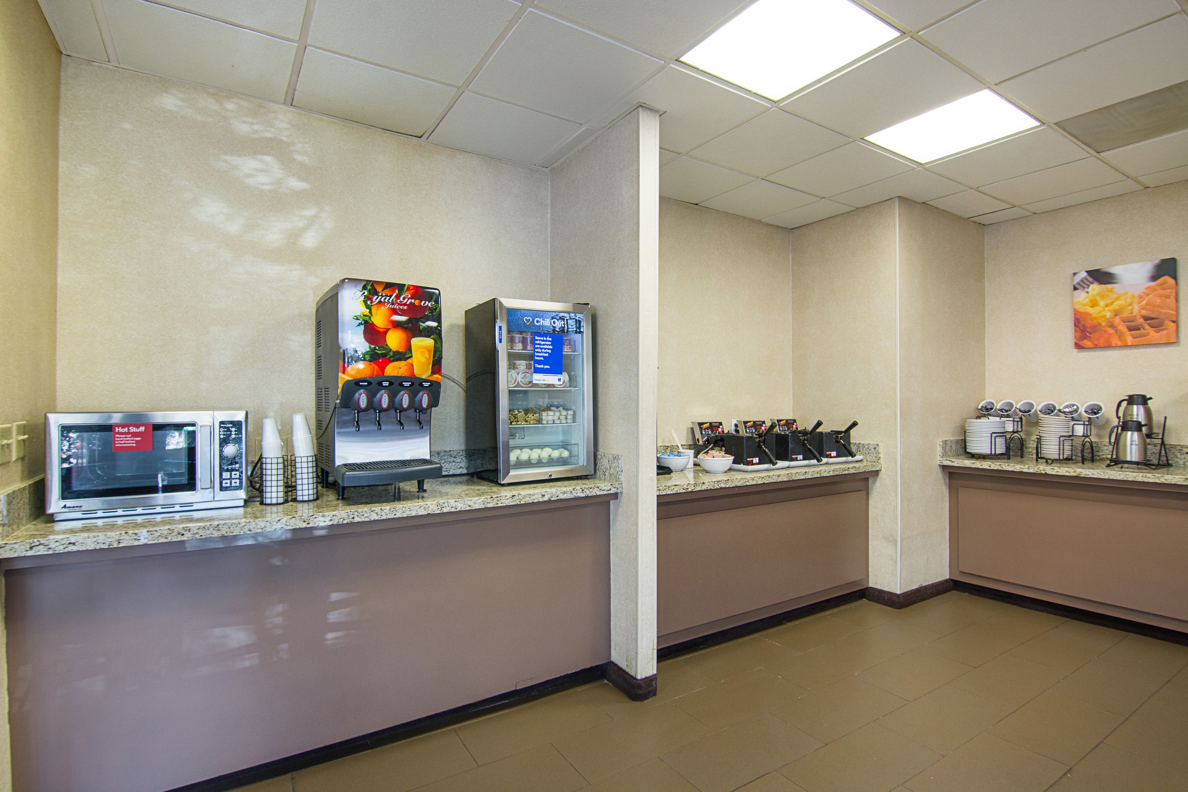 Zona de desayuno autoservicio con microondas, dispensador de jugo y máquina de café.