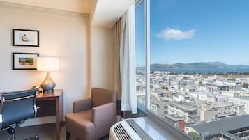 A hotel room with a large window, a desk with a lamp, a chair, and a radiator.