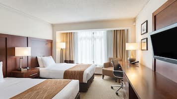 A hotel room with two beds, a desk, a chair, and a television.