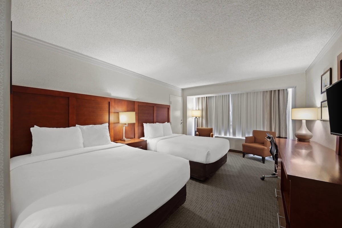 A hotel room with two beds, a desk, a chair, and a TV.