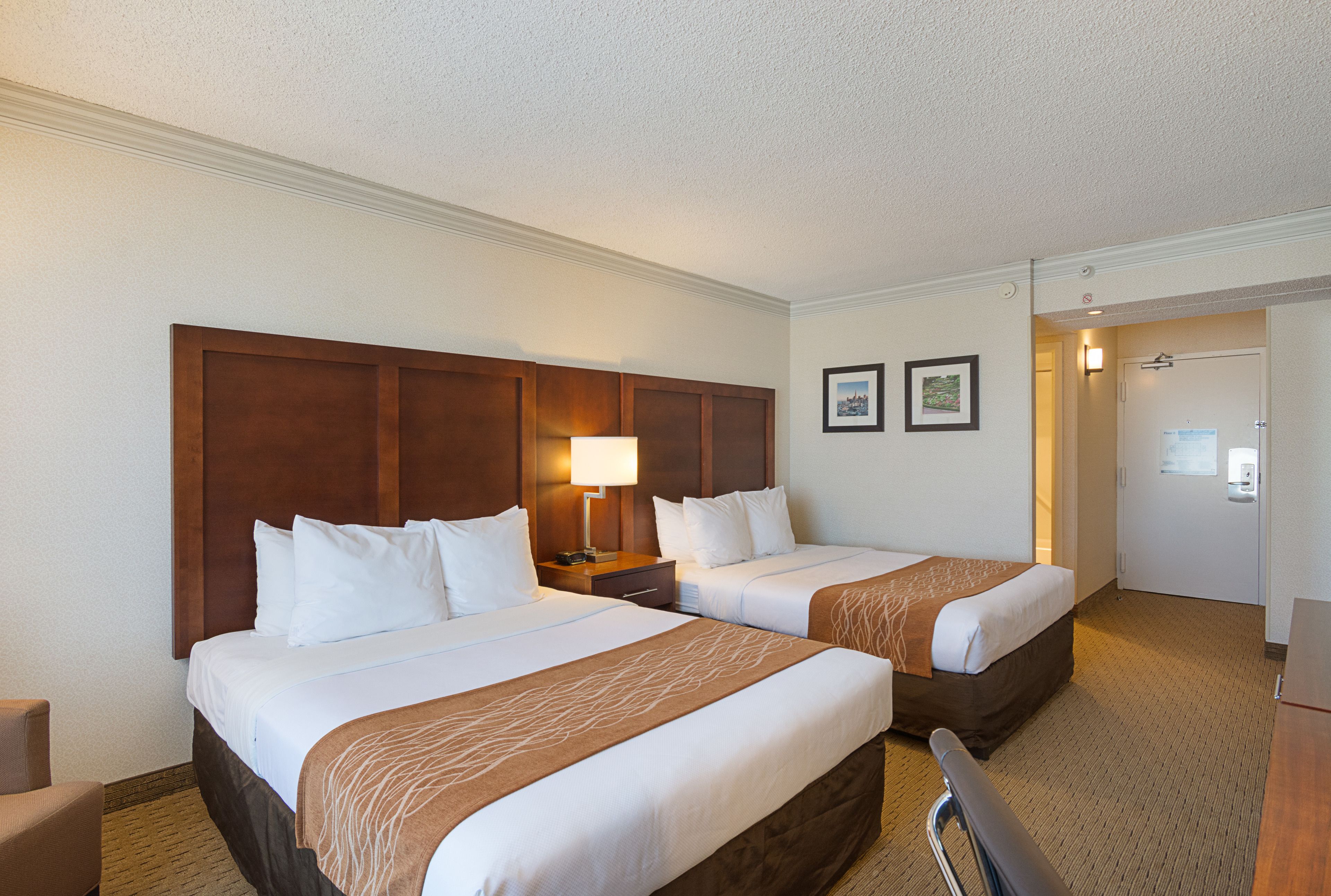 A hotel room with two beds, a desk, a chair, and a door leading to a bathroom.