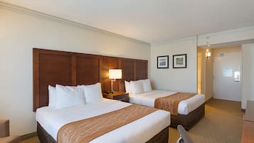 Une chambre d’hôtel avec deux lits, un bureau, une chaise et une porte donnant sur une salle de bain.