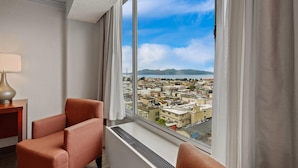 A hotel room with a large window offering a cityscape view, a chair, and a lamp. - Comfort Inn by the Bay (San Francisco)