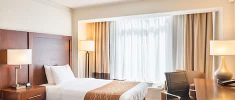 Habitación de hotel con dos camas, un escritorio y una silla. Hay lámparas a ambos lados de las camas y una ventana con cortinas.