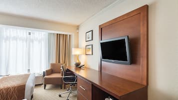 A hotel room with a bed, a desk with a TV, a chair, and a lamp.