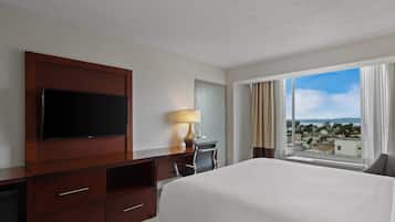 Une chambre d’hôtel avec un grand lit, un téléviseur posé sur un meuble en bois, un bureau avec une lampe et une fenêtre donnant sur la ville.