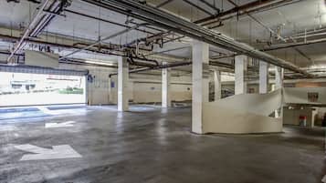 Un estacionamiento interior con pisos de concreto, pilares blancos y tuberías visibles en el techo.