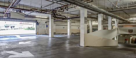 An indoor parking garage with concrete floors, white pillars, and visible ceiling pipes.