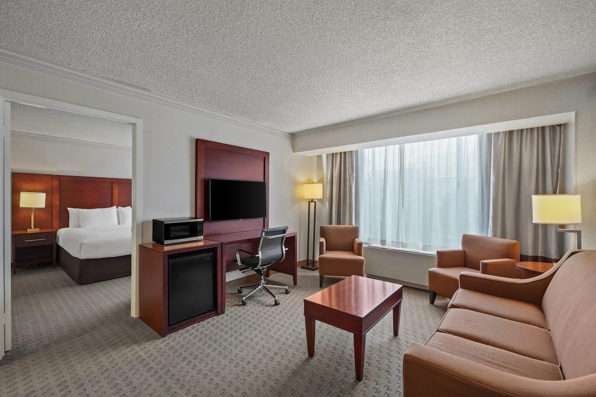 A hotel room with a bed, desk, TV, and seating area.