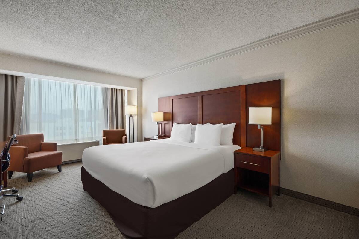 A hotel room with a large bed, two bedside tables, a desk, a chair, and a lamp.