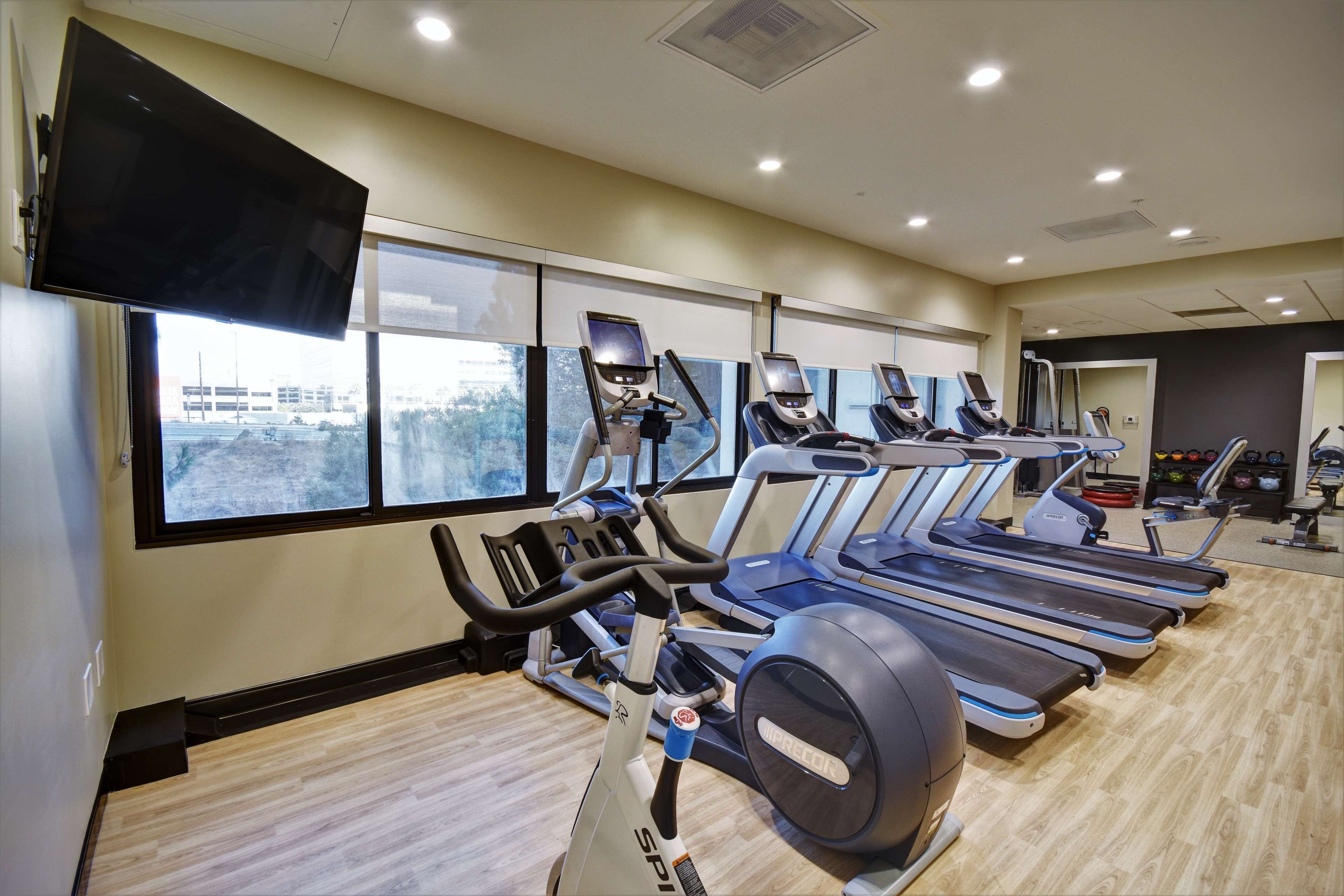 A gym with multiple treadmills, exercise bikes, and a large TV screen.