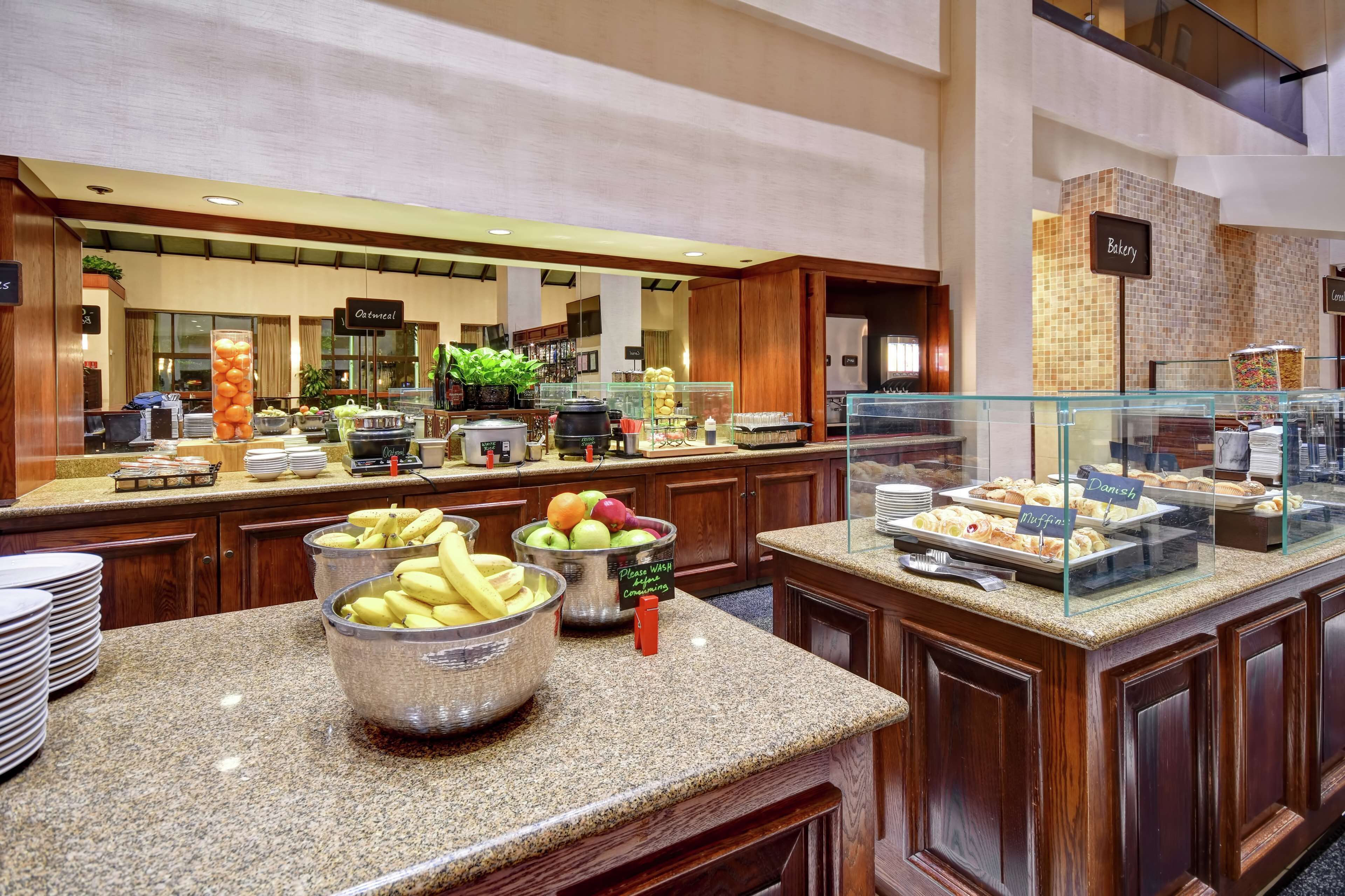 A buffet area with various food options, including fruits and pastries, in a modern hotel setting.