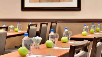 Un salón de conferencias con mesas dispuestas para reuniones, equipado con botellas de agua, vasos y manzanas.