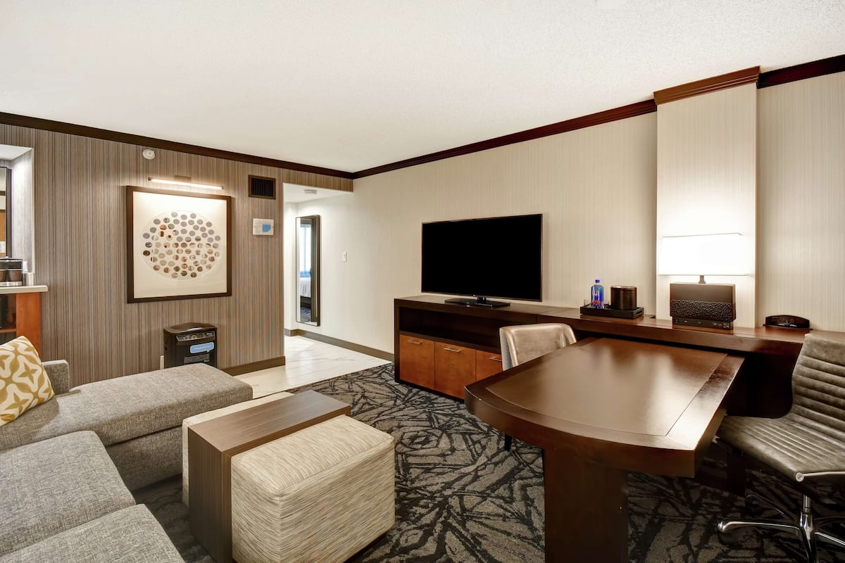 A hotel room with a large bed, a desk with a flat-screen TV, a sofa, and a coffee table.